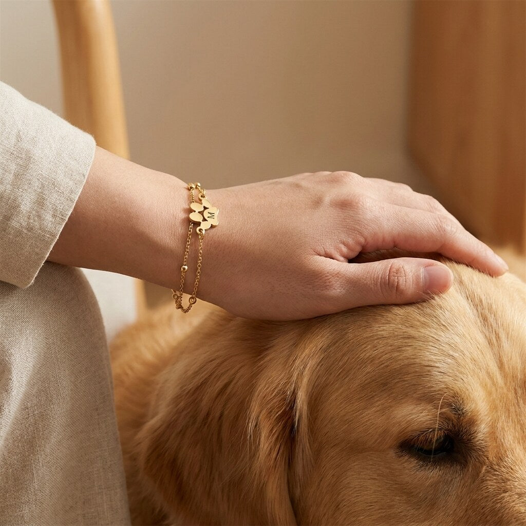 Wrist wearing a gold-tone paw print bracelet while stroking a golden retriever